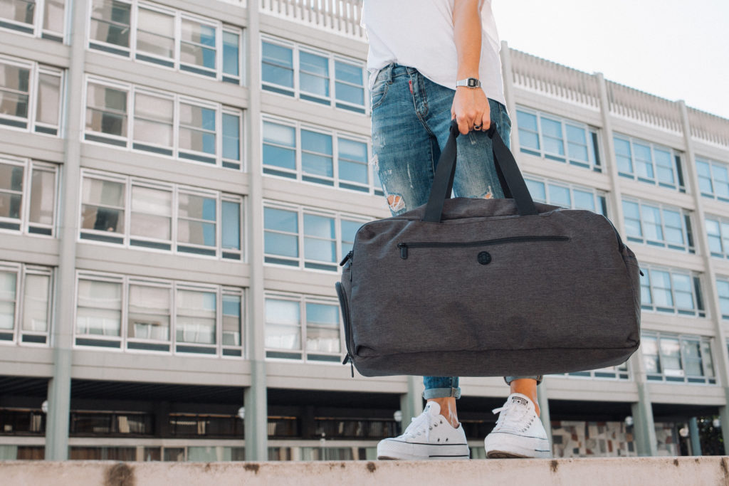 Holding a duffle bag with a building as the background