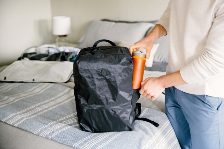 A woman puts a water bottle into an Outbreaker Daypack.