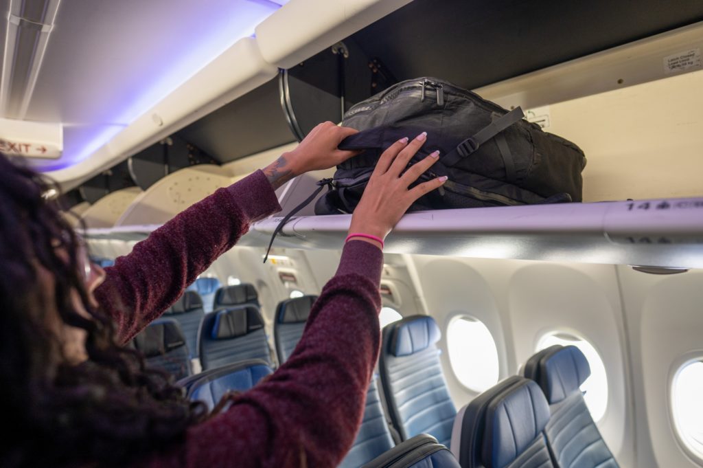 Woman loading backpack into the overhead bin on a plane